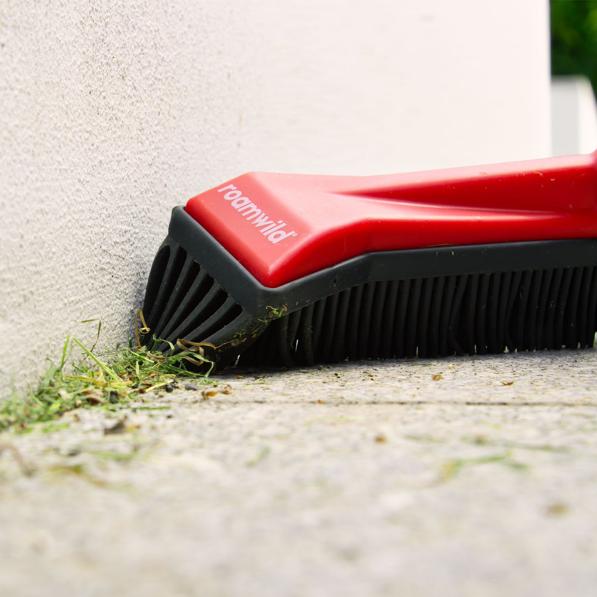Garden broom side blade clearing debris from a wall corner
